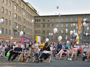 Im Innenhof der Stasi-Zentrale sitzen Zuschauer in Liegestühlen und lassen weiße Ballons starten