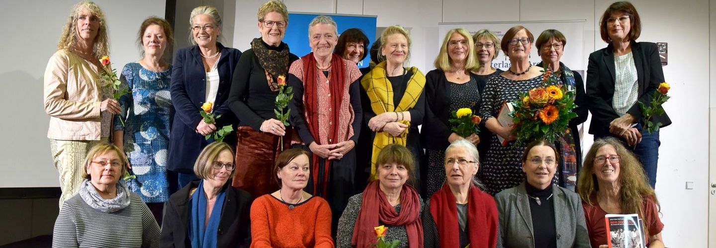 20 Frauen stehen und sitzen auf einer Bühne, viele halten Rosen in der Hand. Das Foto wurde offenbar am Ende der Buchvorstellungsveranstaltung gemacht.