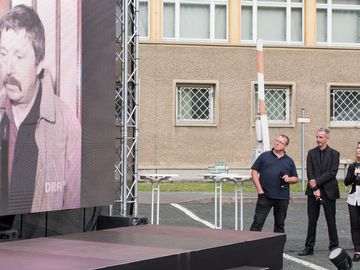 Die Zeitzeugen Michael Heinisch-Kirch und Frank Ebert mit der Moderatorin Dagmar Hovestädt. Links ist eine große Leinwand mit einem alten Foto von Wolf Biermann zu sehen.
