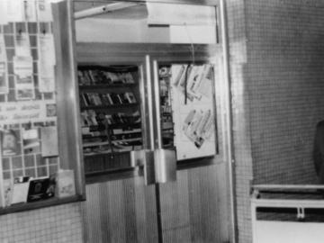 Als Teil einer Fotodokumentation ist auf dem schwarz-weißen Lichtbild die äußere Flügeltür eines Imbiss auf dem Bahnhof zu sehen. Die Fenster sind eingeschlagen.