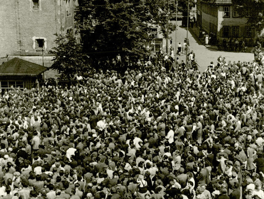 Der Marktplatz von Sömmerda am 17. Juni 1953. Eine große und dichte Menschenmenge ist zu sehen, die sich auf dem Marktplatz drängt. Im Hintergrund ist der Rathausvorplatz zu sehen, der noch weitestgehend ohne Menschen ist.